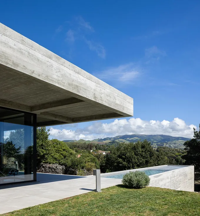 Board-formed concrete roof over a glass wall, with a raised pool and green hills beyond