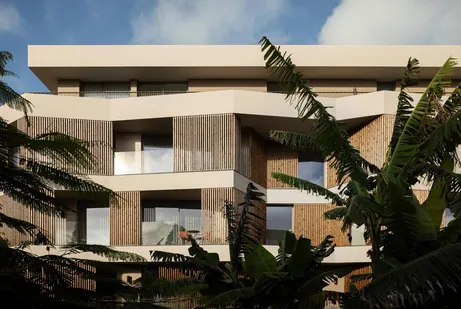 Building with timber slat screens and deep balconies behind banana plants
